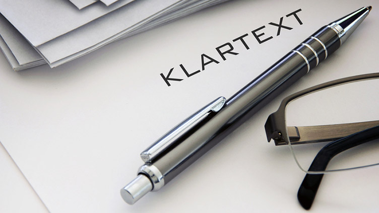 Kugelschreiber, Brille auf Papier, auf dem das Wort "Klartext" steht (Symbolbild für das Tagungsthema Journalismus der Zukunft)