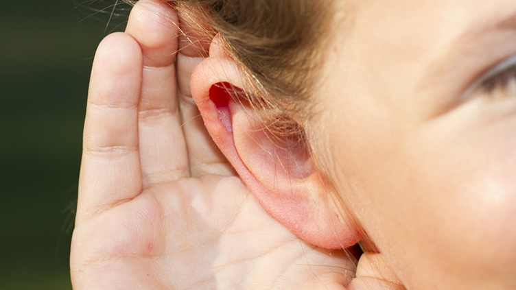 Nahaufnahme: ein Kind hält sich die Hand zum Ohr, damit es besser hören kann.