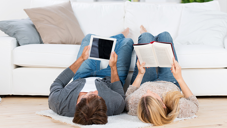 Mann liest ein E-Book und eine Frau liest ein Buch (Symbolild für E-Books in der Büchereiarbeit)
