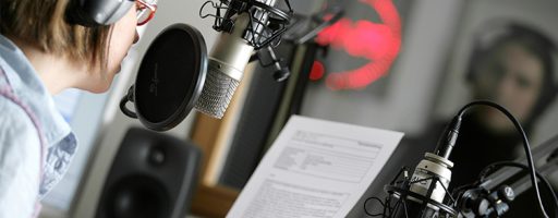 Eine junge Frau sitzt im Studio eines Radiosenders und verliest eine Nachricht über das Mikrofon.