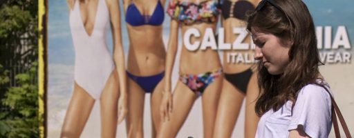 Selbstoptimierung - Anna, die Hauptfigur in der Dokumentation steht vor einer Werbetafel, welche Frauen in makelloser Bikini-Figur zeigt.