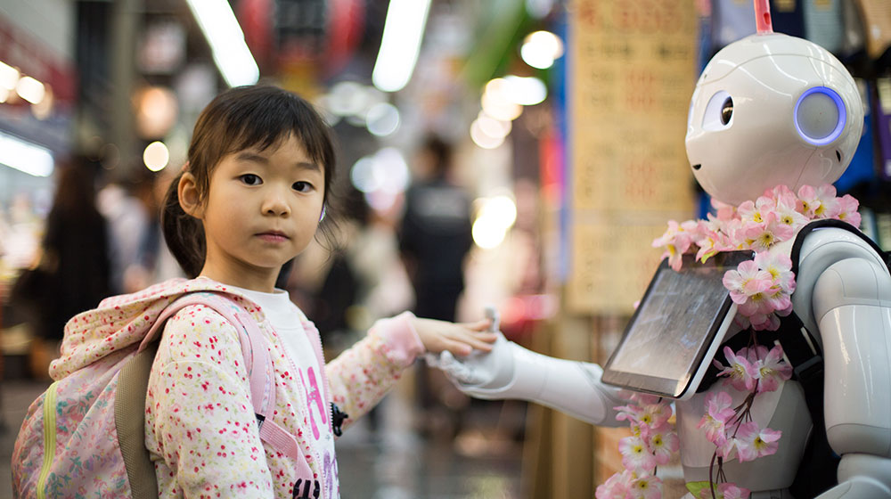Mädchen legt linke Hand in rechte Hand eines Roboters - Digitalität als soziale Frage
