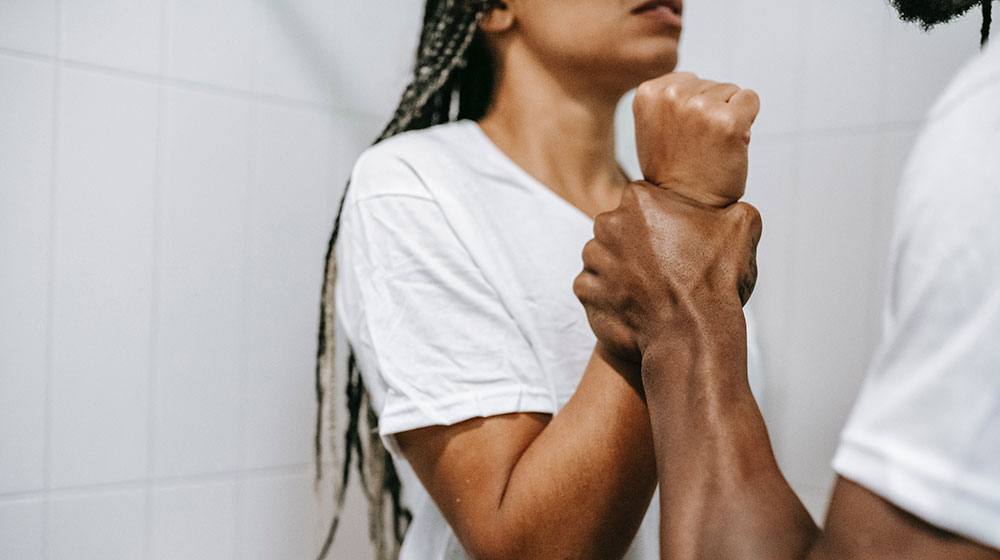 Symbolbild für sexualisierte Gewalt: Gesichtsloser muskulöser ethnischer Mann, der während eines Streits das Handgelenk einer weiblichen Person packt.